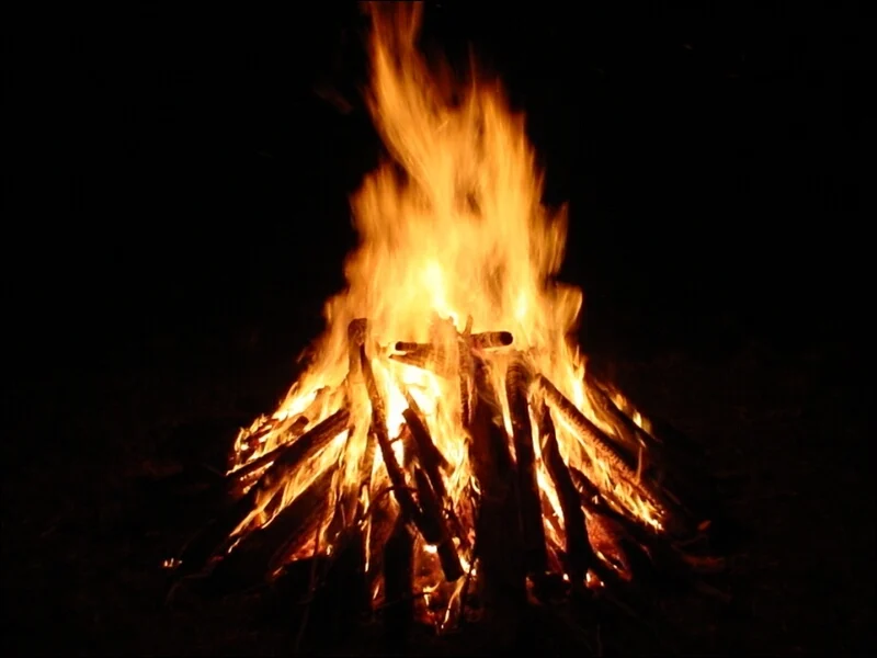 A well-built, classic pyramid-style campfire burning brightly in a wilderness setting, surrounded by logs.